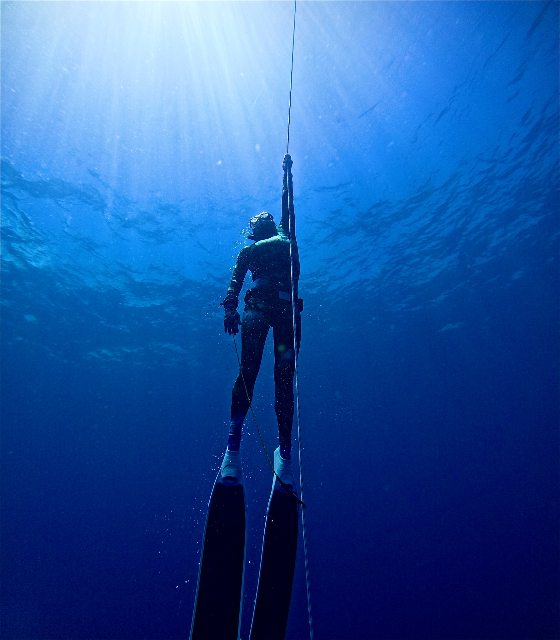 Freediver ascending a line toward sunlight in blue water