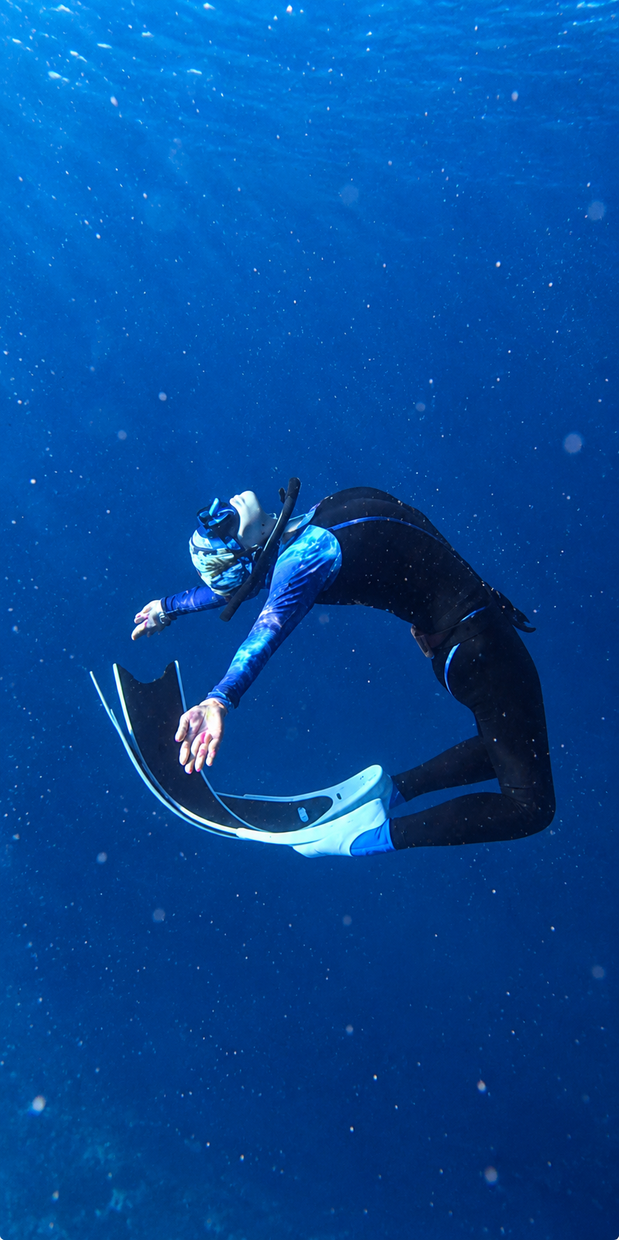 Freediver curled in a relaxed arch in deep blue water