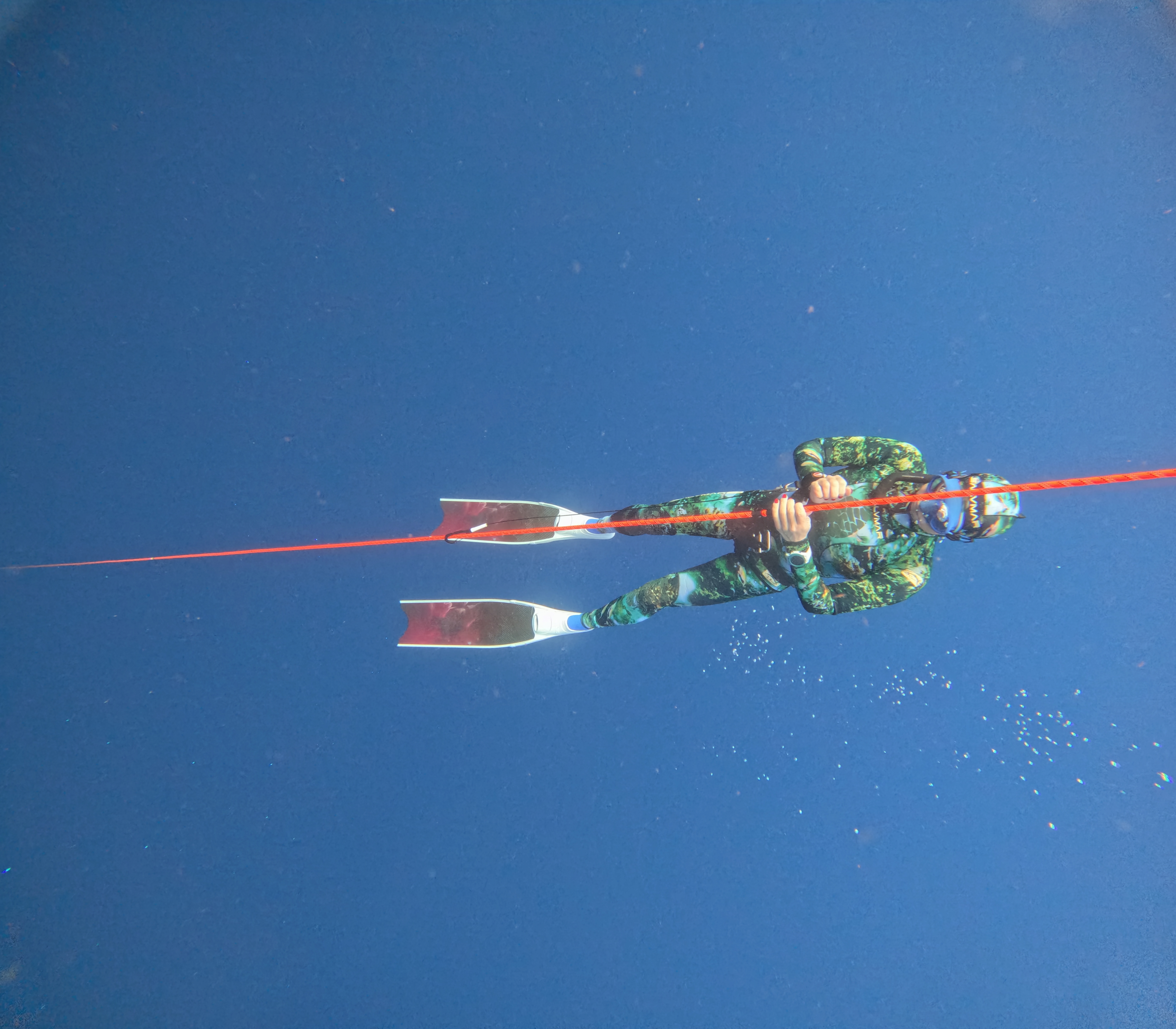 Freediver in a green camouflage wetsuit holding a red guide line